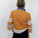 Person wearing a mustard yellow jacket with lace sleeves against a white background