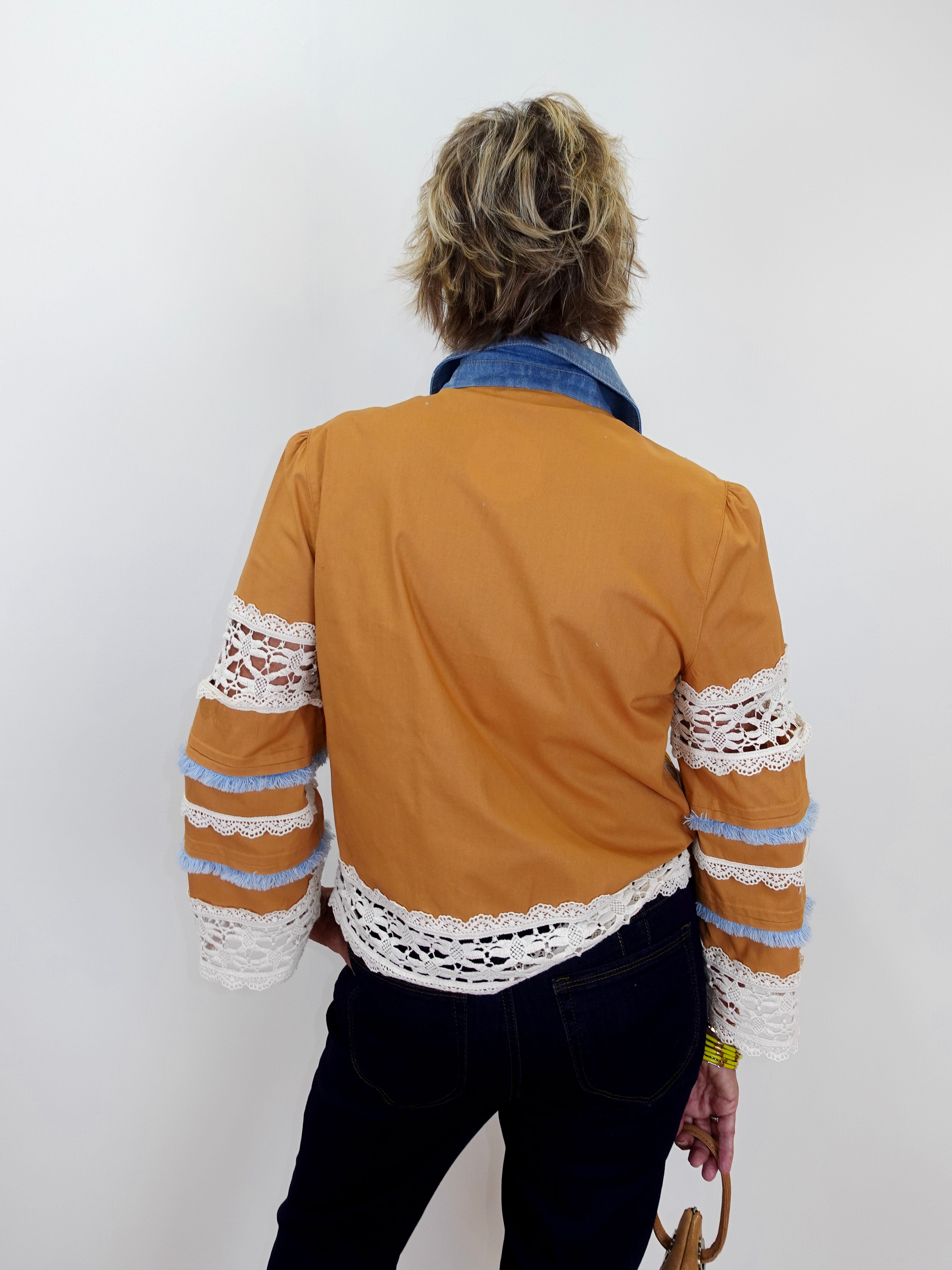 Person wearing a mustard yellow jacket with lace sleeves against a white background