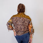 Person wearing a patterned shirt with leopard print and other designs against a white wall.