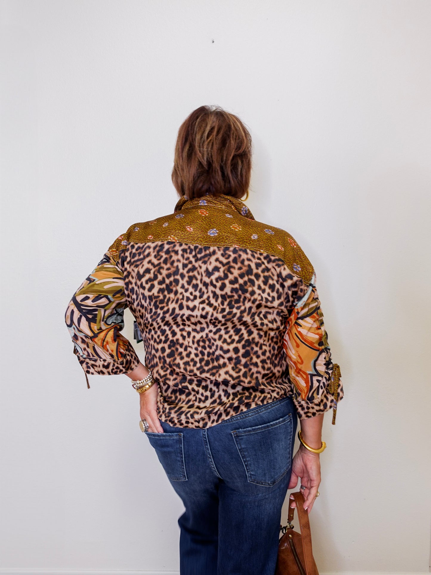 Person wearing a patterned shirt with leopard print and other designs against a white wall.