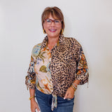 Woman wearing a leopard print shirt over a floral top with blue jeans against a white background