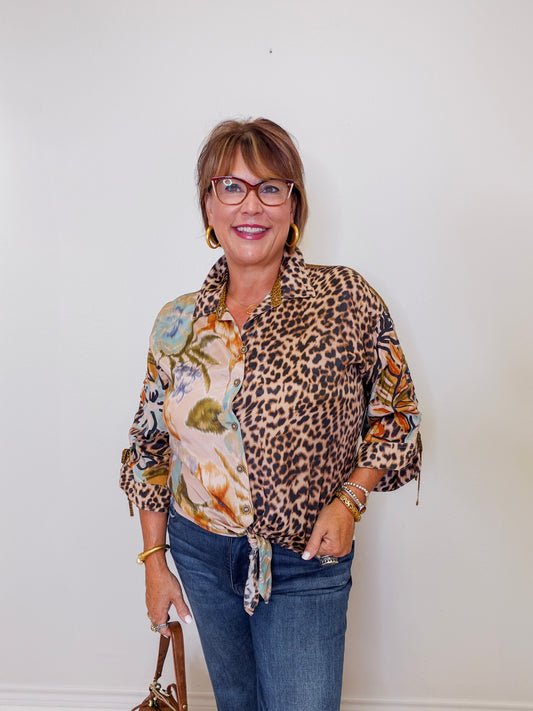 Woman wearing a leopard print shirt over a floral top with blue jeans against a white background