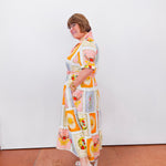 Woman wearing a colorful patterned dress against a white wall.