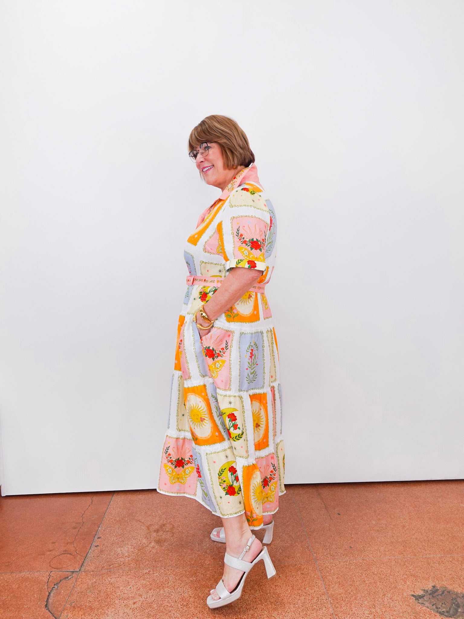 Woman wearing a colorful patterned dress against a white wall.