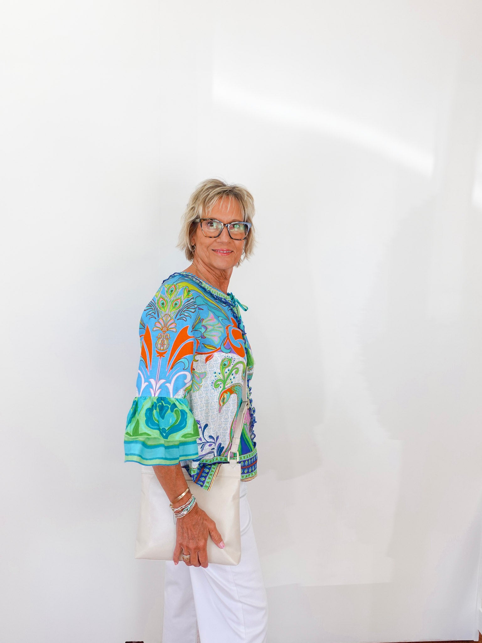 Woman wearing a colorful floral blouse and white pants against a plain background