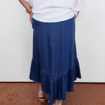 Person wearing a white top and blue denim skirt on a plain background
