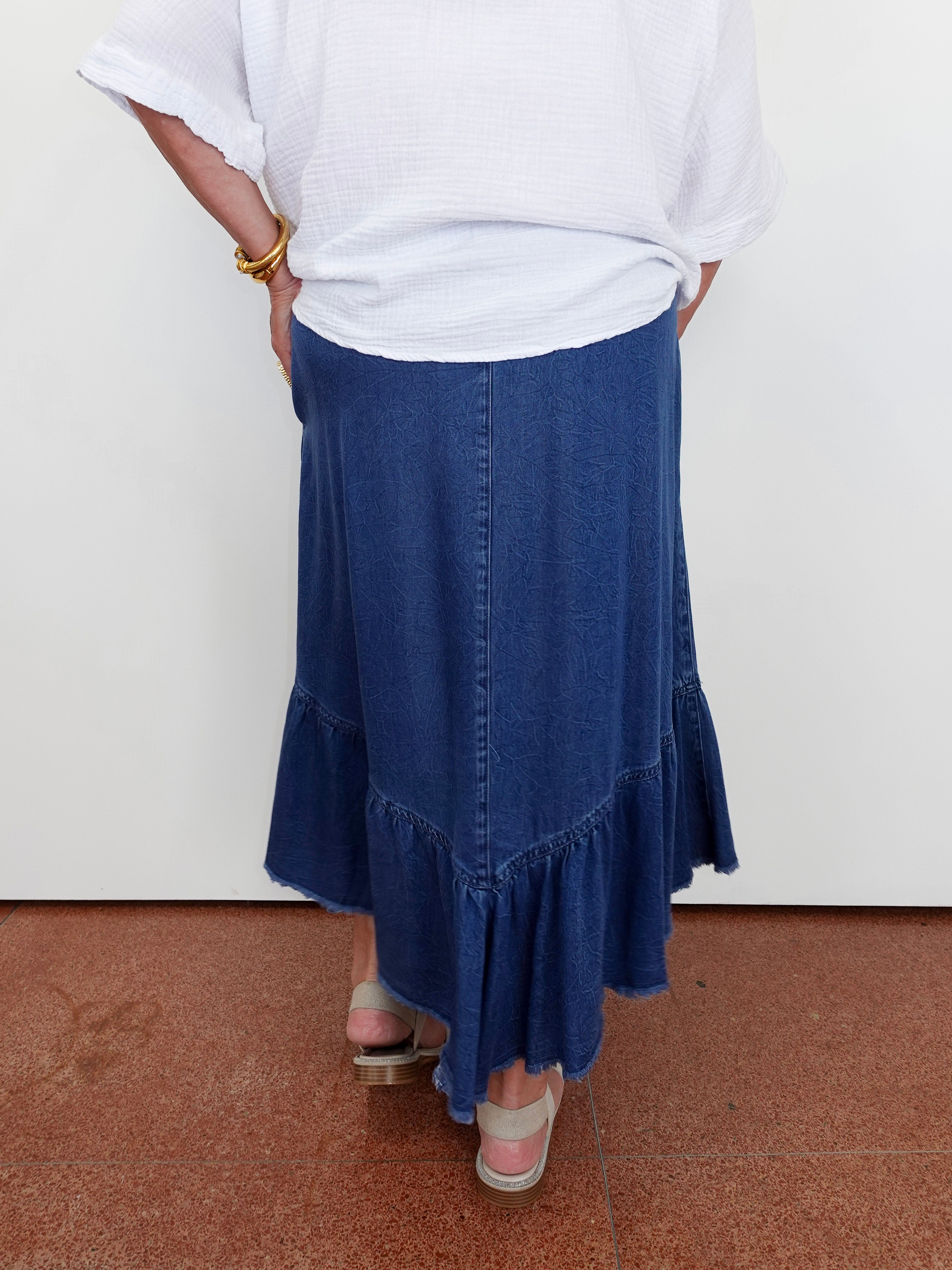 Person wearing a white top and blue denim skirt on a plain background