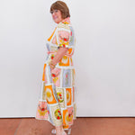 Woman wearing a colorful patterned dress standing against a white wall.