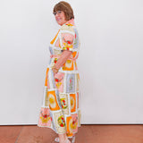 Woman wearing a colorful patterned dress standing against a white wall.