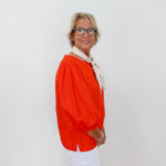 Person wearing an orange blouse and white pants against a plain background