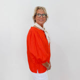Person wearing an orange blouse and white pants against a plain background