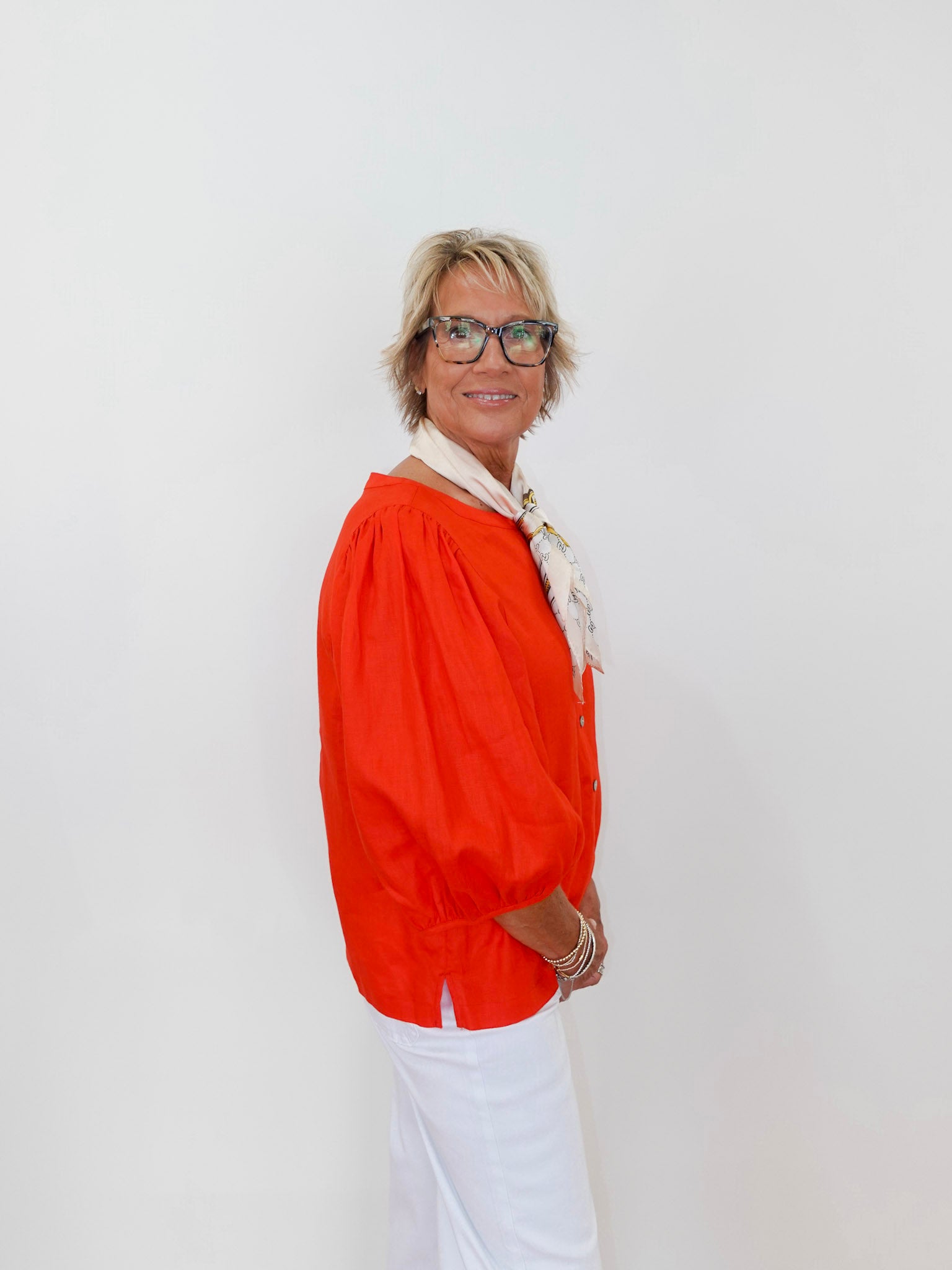 Person wearing an orange blouse and white pants against a plain background