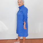 Woman wearing a blue dress standing against a white wall.