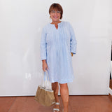 Woman wearing a light blue dress holding a beige handbag indoors.