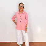 Person wearing a pink shirt, white pants, and green shoes against a white wall.