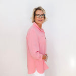 Person wearing a pink shirt and white pants against a plain background