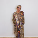 Person wearing a leopard print outfit with a colorful scarf against a white wall.