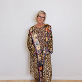 Person wearing a leopard print outfit with a colorful scarf against a white wall.