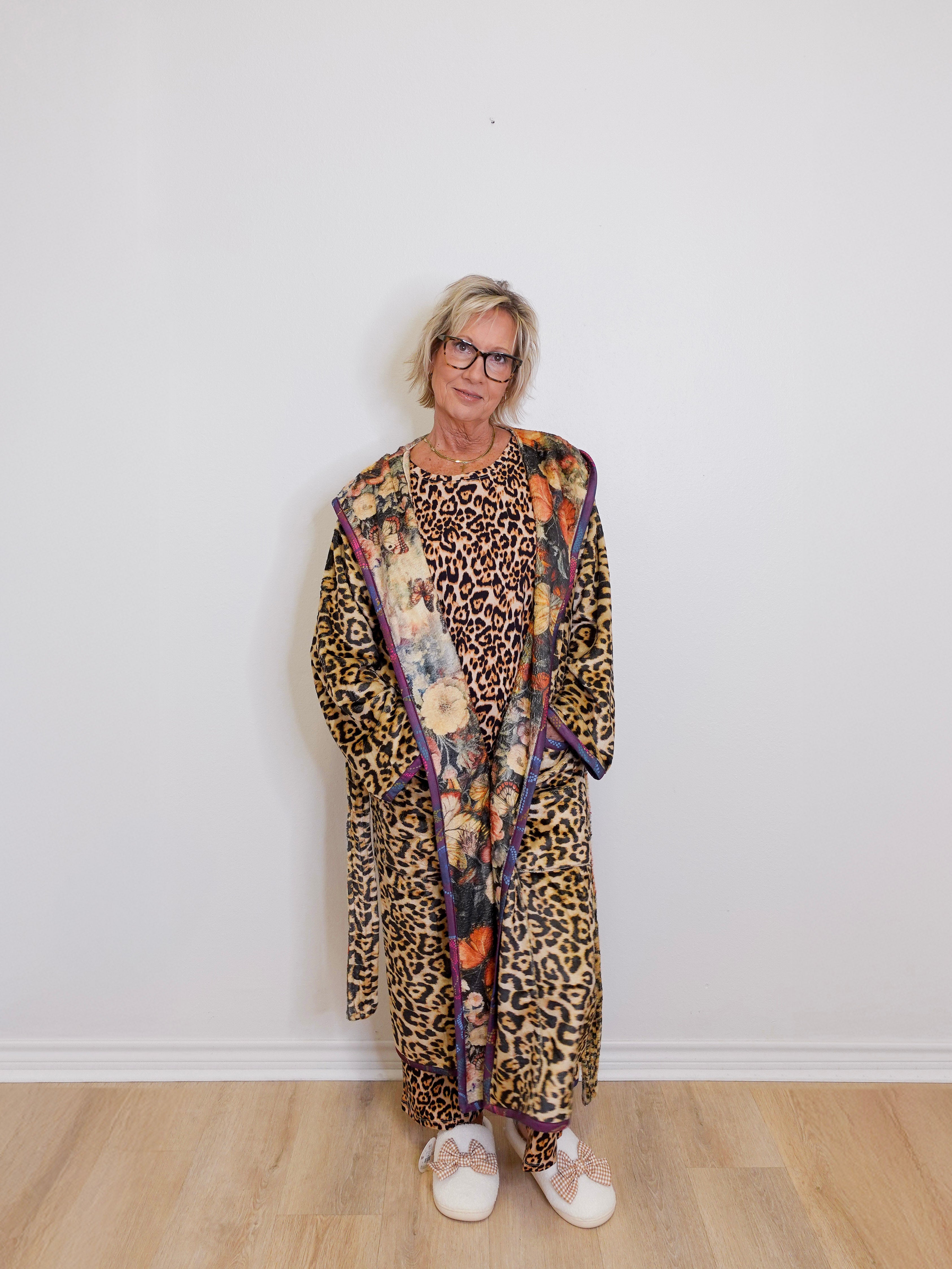 Person wearing a leopard print outfit with a colorful scarf against a white wall.