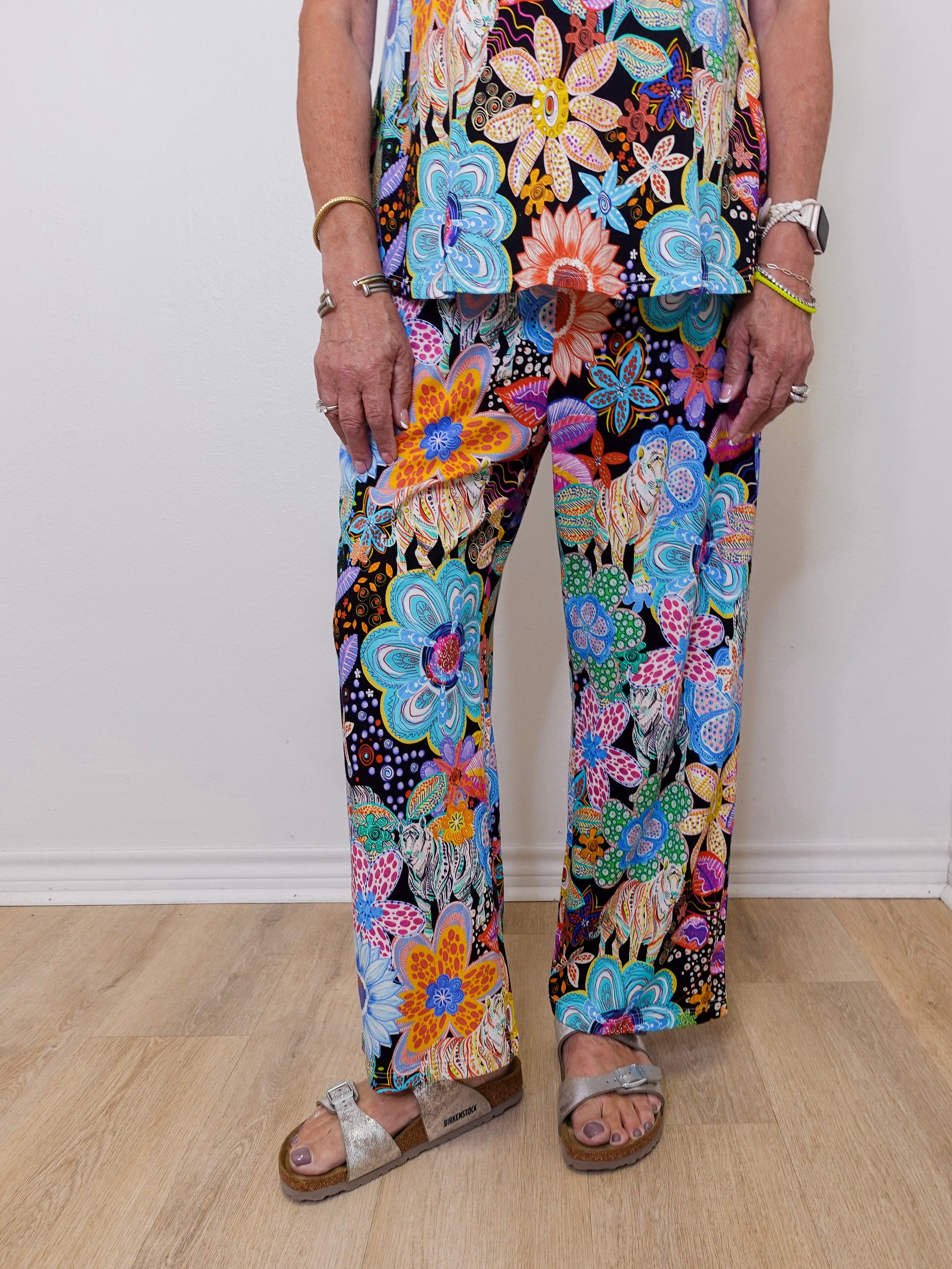 Person wearing colorful floral pants on a wooden floor.
