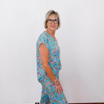 Woman wearing a blue floral outfit standing against a white wall.