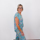 Woman wearing a blue floral outfit standing against a white wall.
