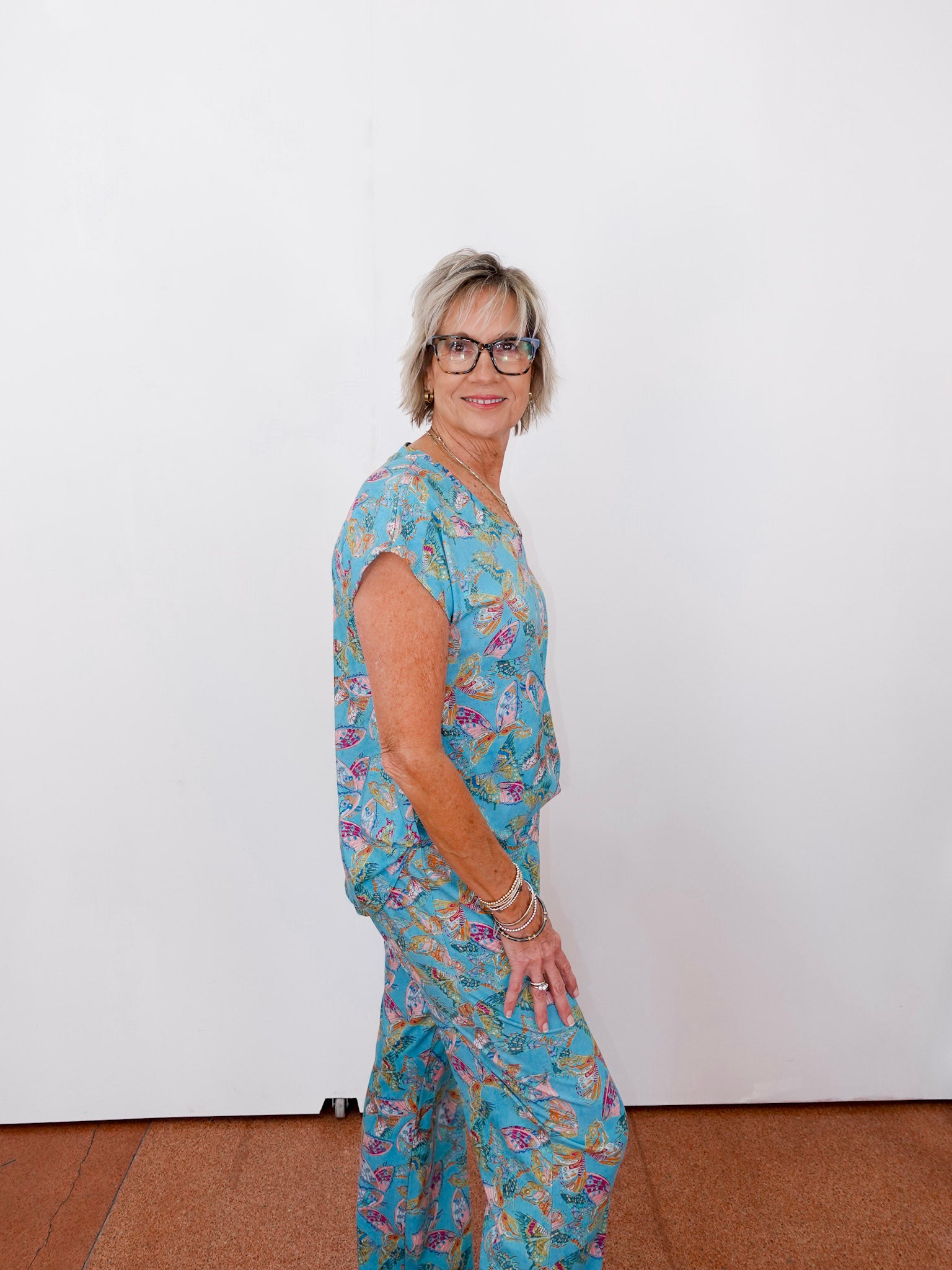 Woman wearing a blue floral outfit standing against a white wall.