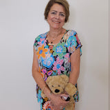 Woman in a colorful floral dress holding a teddy bear against a plain background