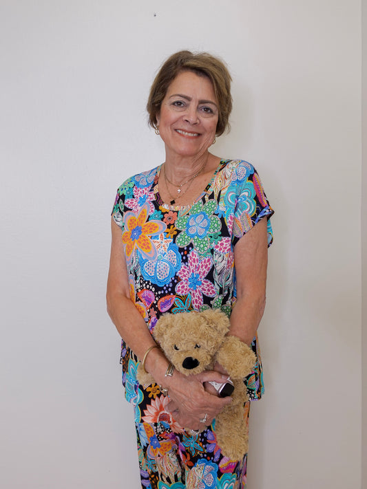 Woman in a colorful floral dress holding a teddy bear against a plain background