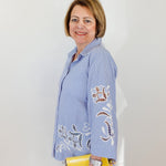 Woman wearing a blue embroidered shirt holding a yellow clutch against a white background