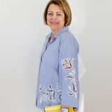 Woman wearing a blue embroidered shirt holding a yellow clutch against a white background