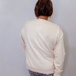 Person wearing a cream sweatshirt and patterned pants against a white wall
