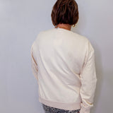 Person wearing a cream sweatshirt and patterned pants against a white wall