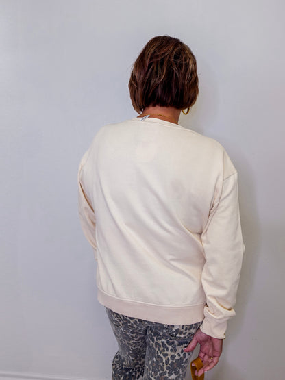Person wearing a cream sweatshirt and patterned pants against a white wall