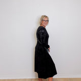 Woman wearing a black dress standing against a white wall.