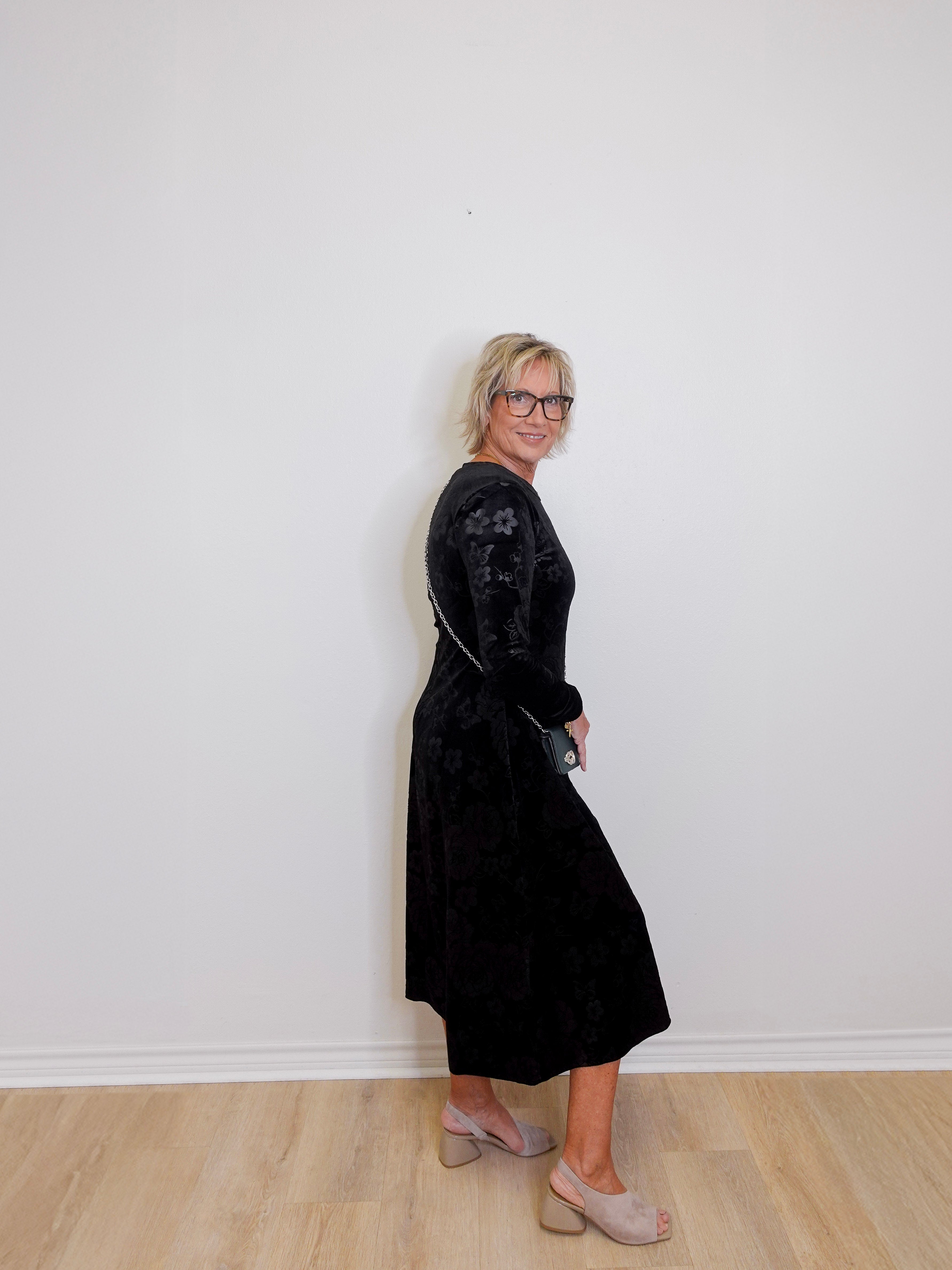 Woman wearing a black dress standing against a white wall.