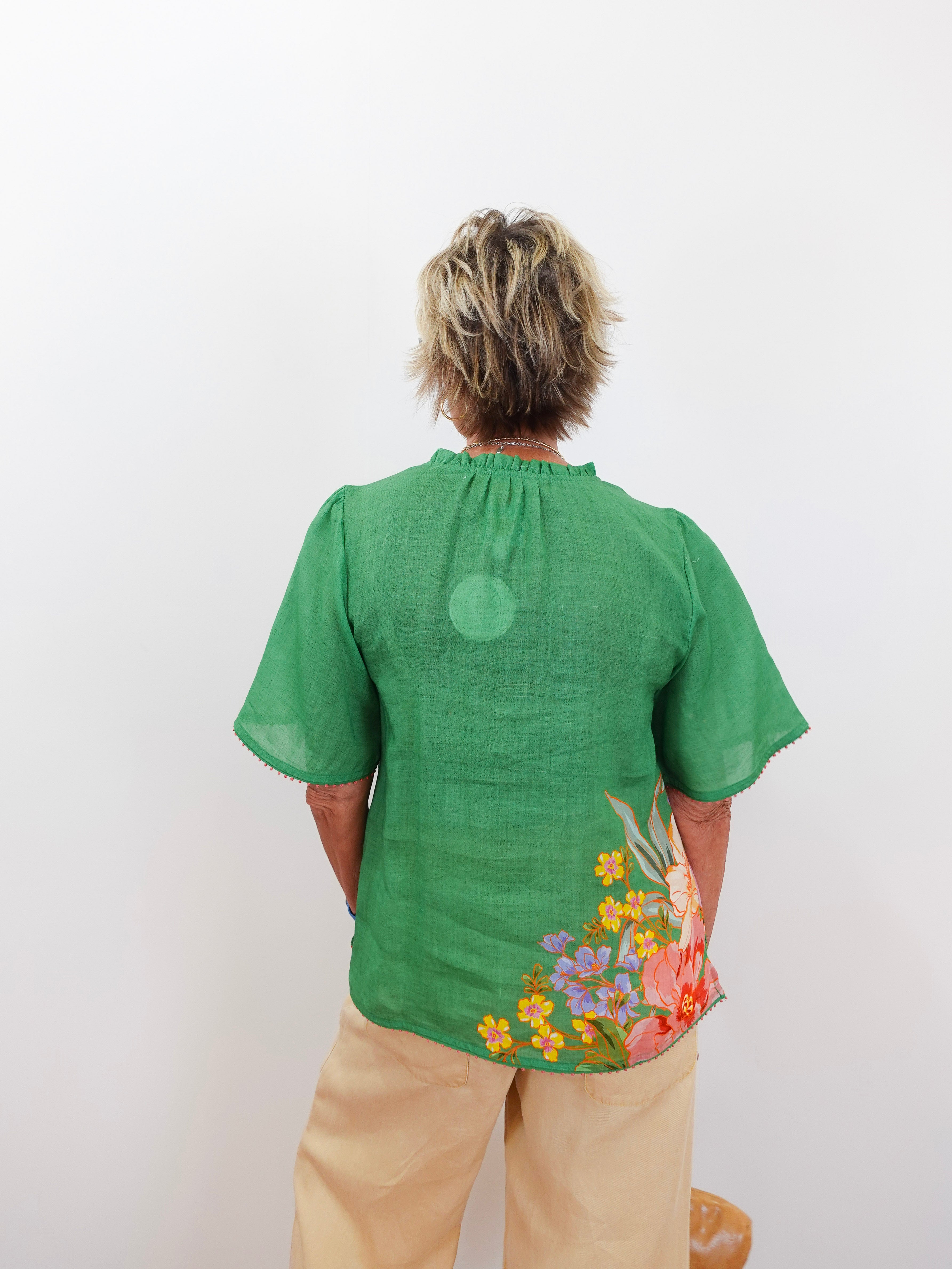 Person wearing a green blouse with floral designs on the back, standing against a white background