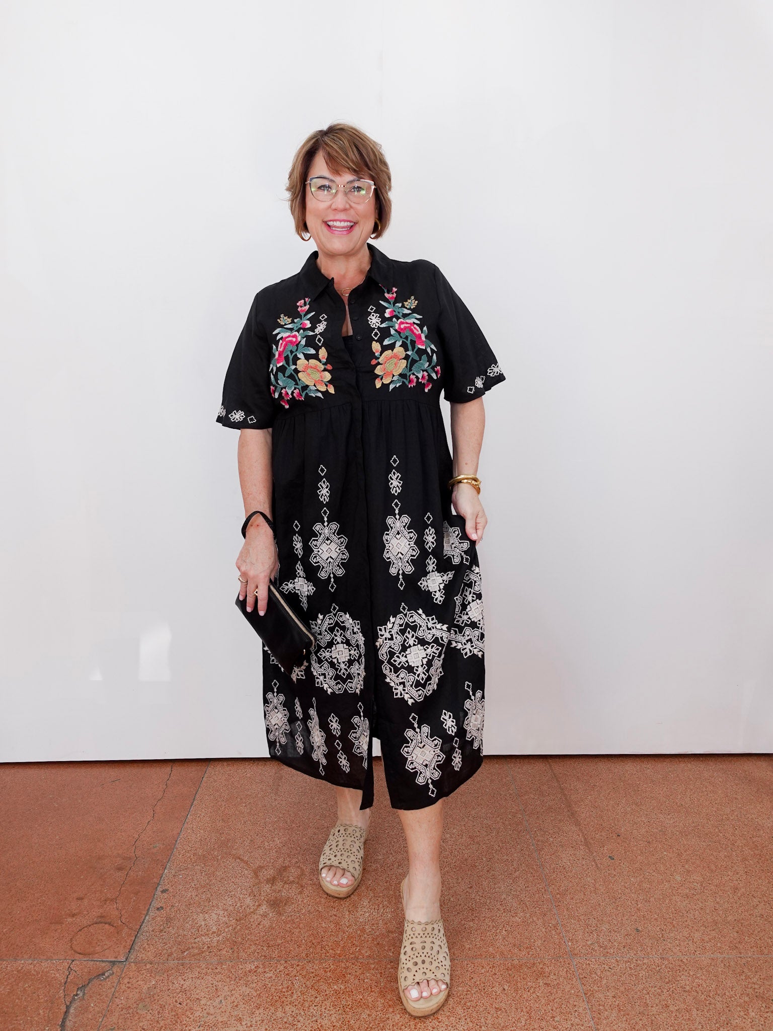 Woman wearing a black dress with floral patterns against a white wall.