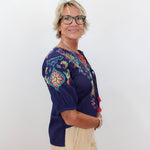 Woman wearing a colorful embroidered top against a white background