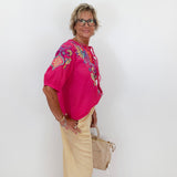 Woman wearing a pink embroidered blouse and beige pants against a white background