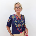 Woman wearing a colorful embroidered blouse with a plain background