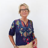 Woman wearing a colorful embroidered blouse with a plain background