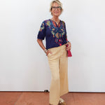 Person wearing a colorful blouse and beige pants against a white wall.
