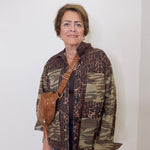 Woman wearing a camouflage and leopard print jacket with a brown bag against a white background