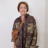 Woman wearing a camouflage and leopard print jacket with a brown bag against a white background