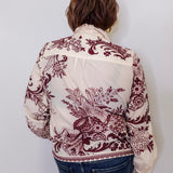 Person wearing a white blouse with red floral patterns against a plain background