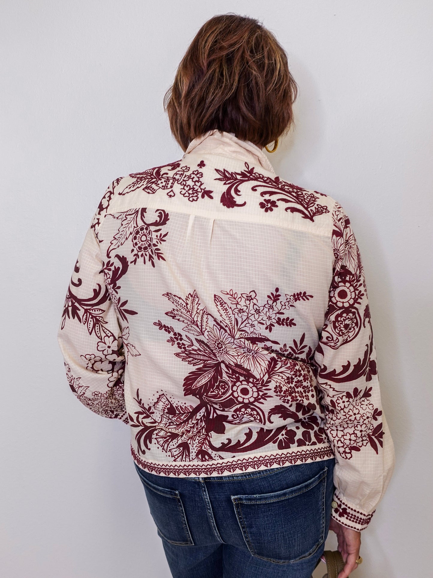 Person wearing a white blouse with red floral patterns against a plain background