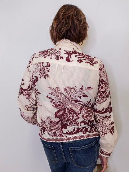 Person wearing a white blouse with red floral patterns against a plain background