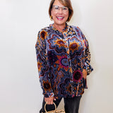 Woman wearing a patterned blouse holding a beige handbag against a white background