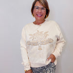 Woman wearing a cream sweatshirt with decorative elements against a white wall